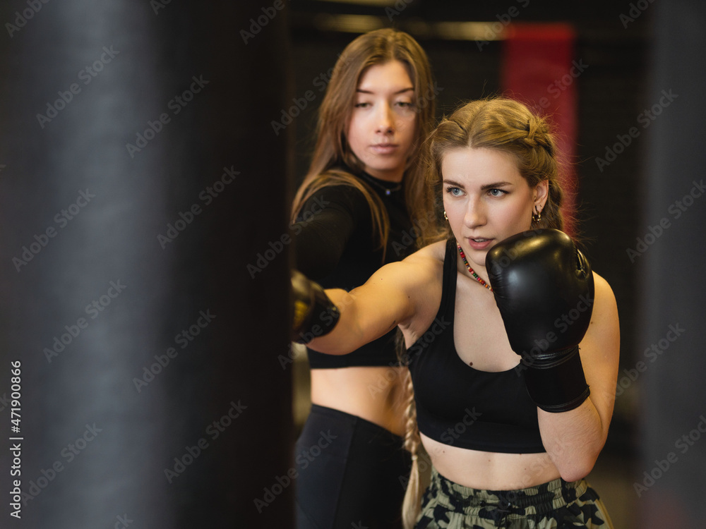 Women's fitness boxing workout in the gym. The blonde sportswoman, under the guidance of a trainer, performs blows on a punching bag.