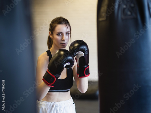 Women's fitness boxing workout in the gym. Skinny young woman performs punching bag punches.