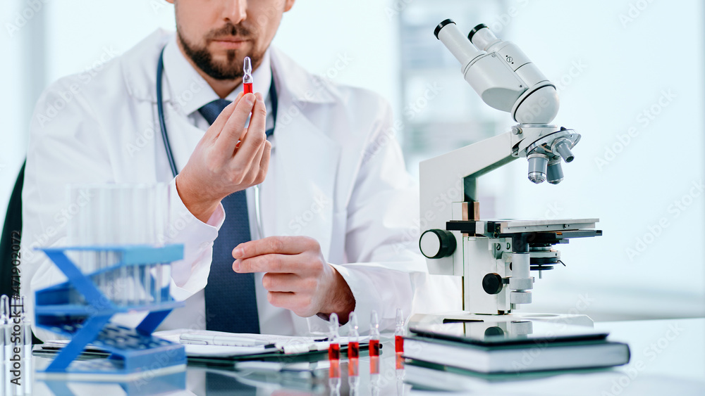 Fototapeta premium scientific researcher with an ampoule of vaccine, sitting at a laboratory table.