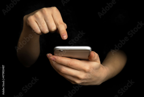 Person uses mobile phone with index finger. Hand with modern smartphone on a black background, communication and techonology concept photo