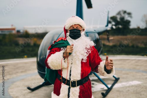 Happy Santa Claus with protective face mask arrives via helicopter to deliver presents to children.