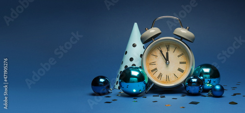 Alarm clock with party hat and Christmas balls on blue background with space for text