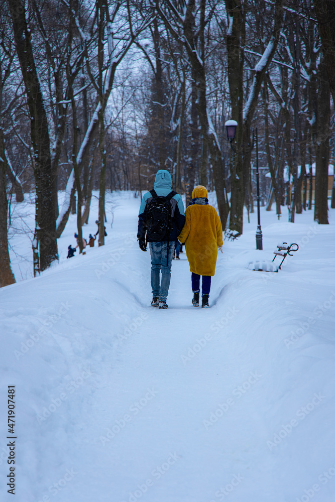 December winter park with a lot of snow, ordinary outdoor view, two person boy and girl walking with holding hands back to camera, vertical photo, focus on backs