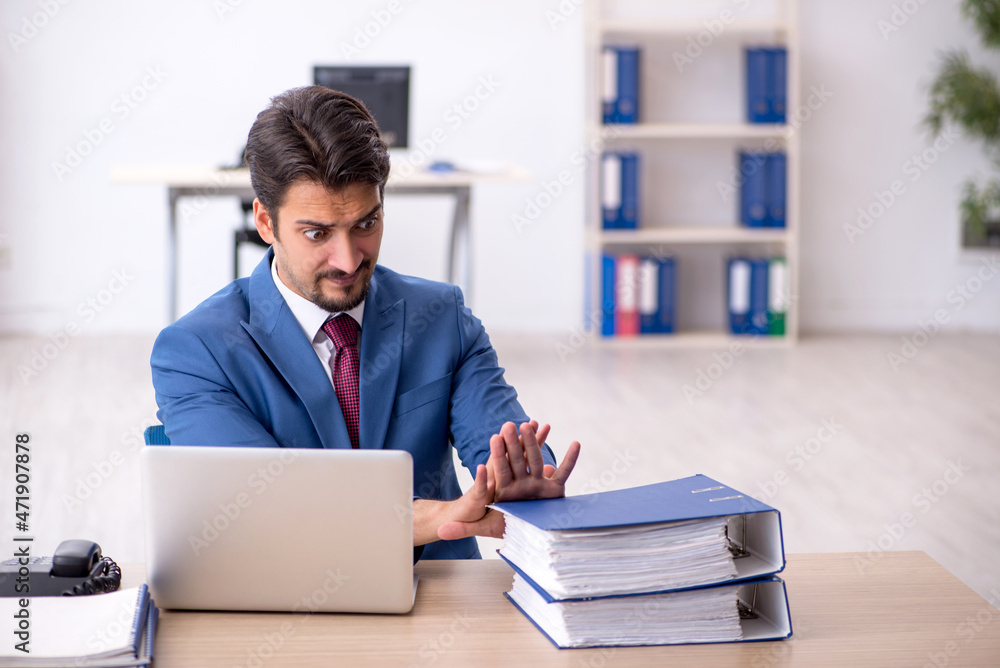 Young male employee unhappy with excessive work in the office Young male employee unhappy with excessive work in the office