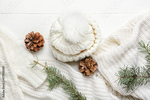 Warm clothes with fir cones and branches on white wooden background