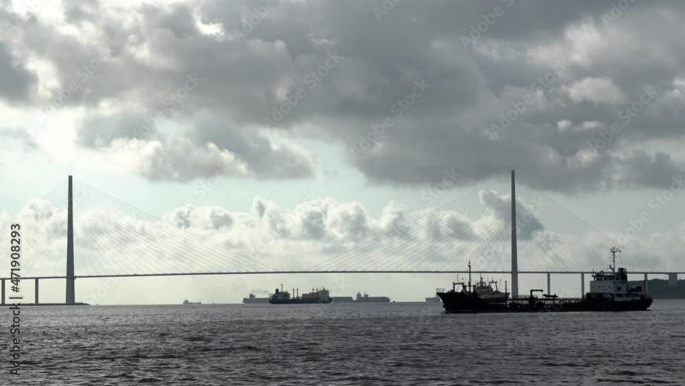 Ships under the bridge. Ship sails by in silhouette. Bunkering vessel. Huge cable-stayed bridge. Many vessels in silhouette. Monochrome. View from water Ships under the bridge. Ship sails by in silhouette. Bunkering vessel. Huge cable-stayed bridge. Many vessels in silhouette. Monochrome. View from water