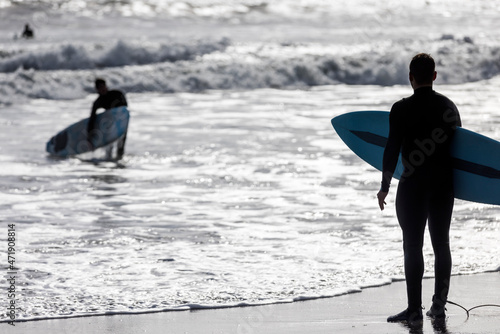 Silhouette of a surfer holding a board watching other people out catching waves on the Califonia coast photo