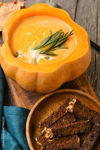 Tasty soup served in pumpkin with bread on wooden background