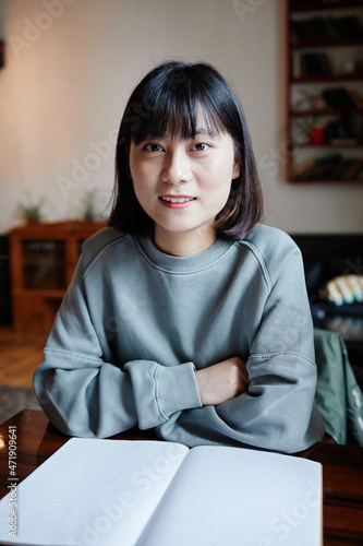 Portrait of college student smiling at camera while sitting at the table with book preparing for homework