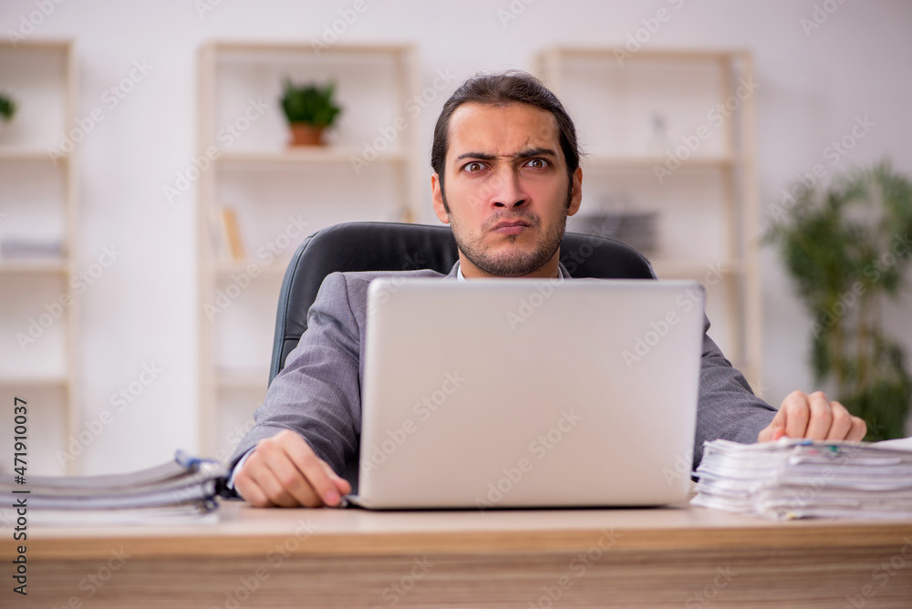 Young male employee unhappy with excessive work in the office Young male employee unhappy with excessive work in the office