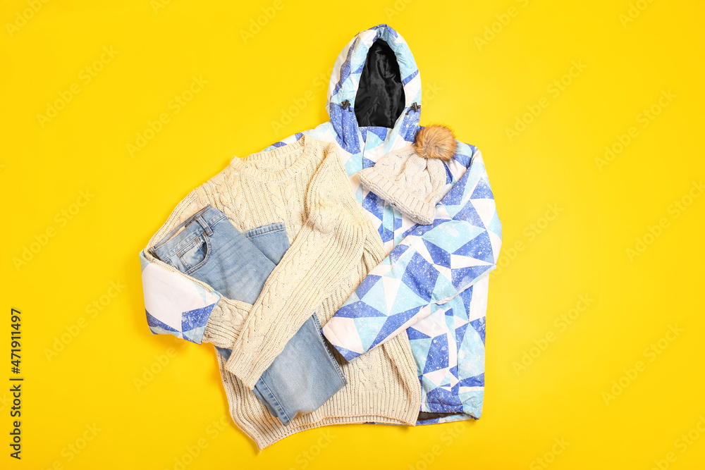 Stylish down jacket, sweater, jeans and hat on color background Stylish down jacket, sweater, jeans and hat on color background
