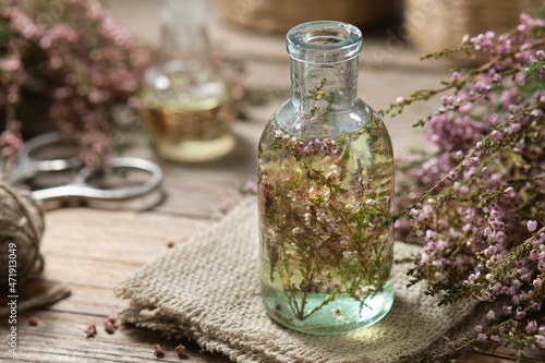 Bottle of heather essential oil or infusion, bunch of Calluna vulgaris flowers on background. Alternative herbal medicine. photo