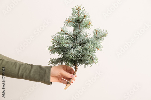 Female hand with fir tree branch on beige background, closeup