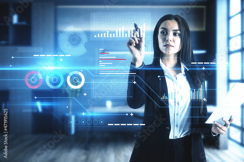 Portrait of attractive young european businesswoman using digital business chart interface on blurry office interior background. Finance, trade, technology and future concept. Double exposure.