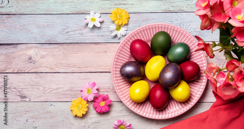 Colorful panted Easter eggs on pink plate and pastel color background with flowers. Easter spring holidays
