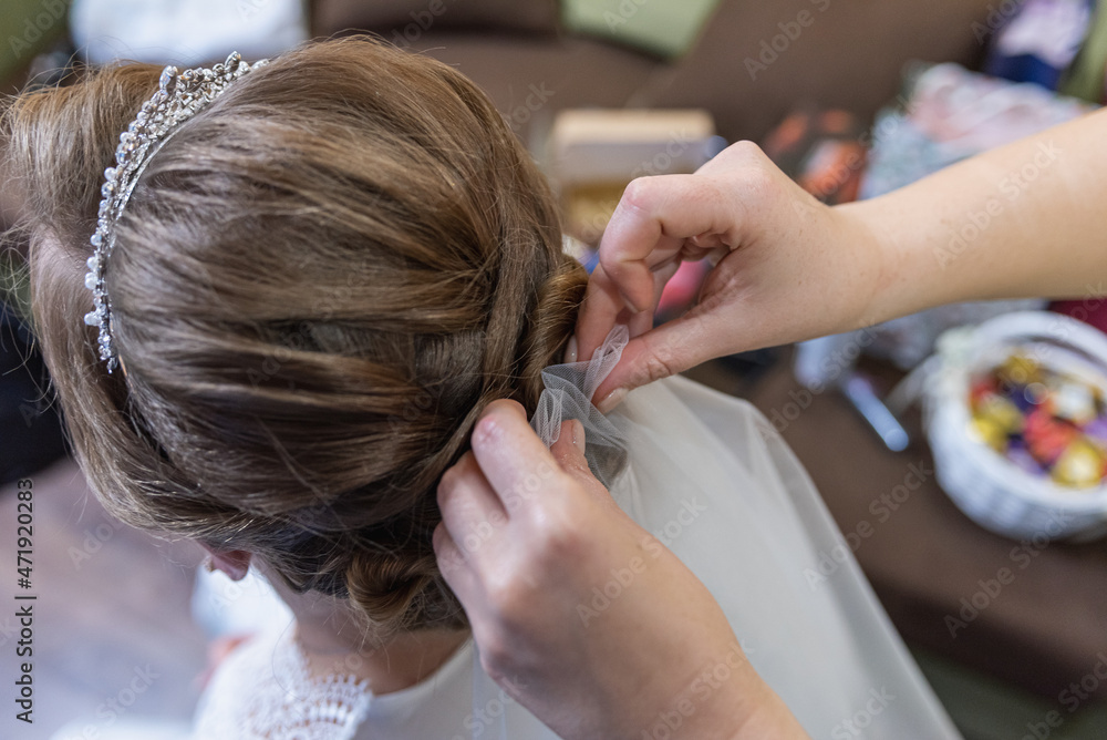 Naklejka premium Hairdresser makes hairstyle wedding for long hair bride on the morning of closeup rear view