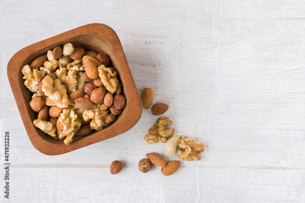Variety of walnuts in wooden bowl. Hazelnuts, walnuts, pecans, pine nuts, peanuts, macadamia, almonds, Brazil nuts. Food mix on white background top view. Copy space Variety of walnuts in wooden bowl. Hazelnuts, walnuts, pecans, pine nuts, peanuts, macadamia, almonds, Brazil nuts. Food mix on white background top view. Copy space