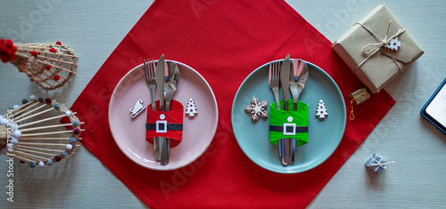 Top view of Christmas tables setting, cutlery and DIY napkin ring holders like Santa clothes made with toilet paper rolls, festive dinner for family with kids. Ecological and sustainable celebration