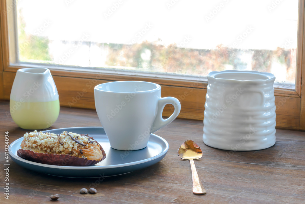 white espresso coffee cup, fresh baked eclair sweet dessert on plate kitchen table against window, utensils dishware, milk jug, home green plant. morning french home breakfast, copy space