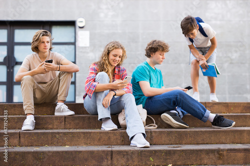 Group of teens gathered together on stairs beside school building and using their smartphones.