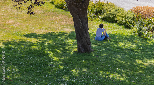 Woman sitting under tree reading a book in sunny day.