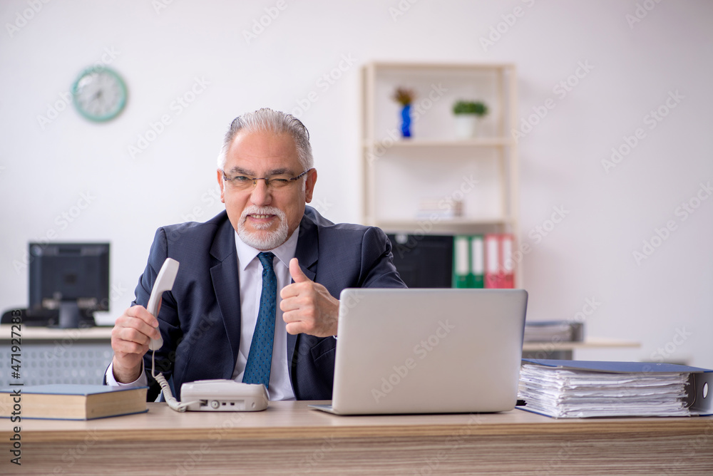 Old male employee speaking on the phone at workplace Old male employee speaking on the phone at workplace