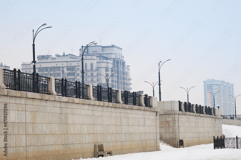Obraz premium Houses on the embankment of the Amur River during a snowfall. Winter morning. Granite walls. Snow falls. Blagoveshchensk, Amur region, Russia.