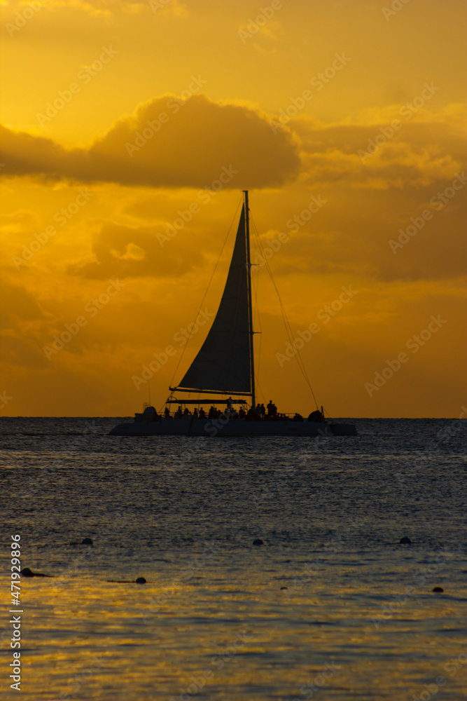 SUNSET ON THE BEACH WITH BOATS IN THE ORIZON AND ORANGE SUNLIGHT, WITH BLUE SKY AND SOME CLOUDS