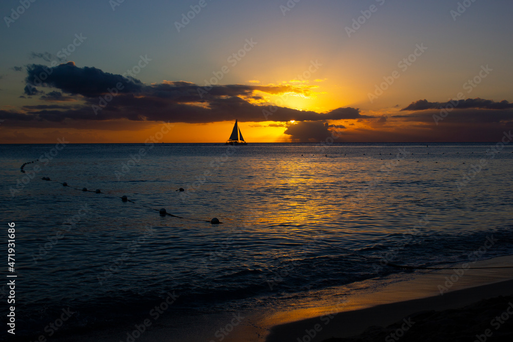 SUNSET ON THE BEACH WITH BOATS IN THE ORIZON AND ORANGE SUNLIGHT, WITH BLUE SKY AND SOME CLOUDS