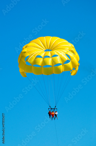 Back view of a Yellow parasailing with 3 people in Punta Cana. Clear sunny blue sky day