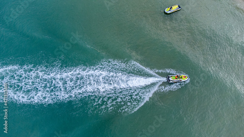 Aerial bird eyes view of jet ski boat cruising in high speed in turquoise clear water sea. © chayakorn