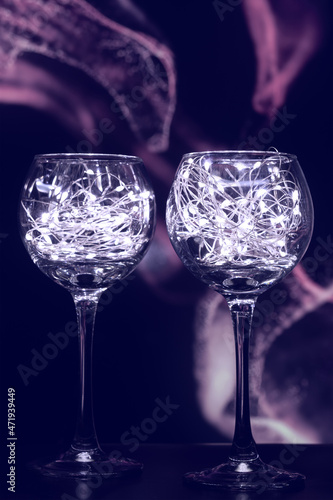 The wine glasses are made of transparent glass, filled with bright lights. Two wine glasses filled with glowing lights of garlands. Interesting, bright, festive background, for holidays.
