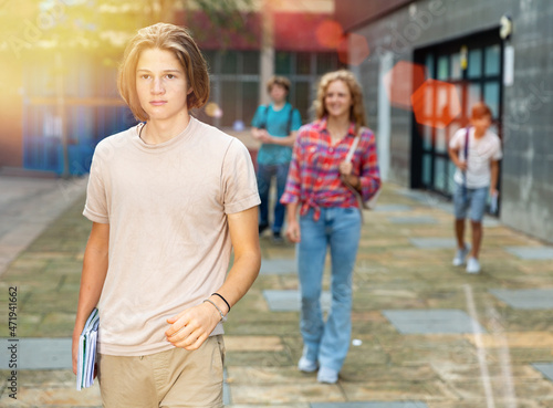 Positive teen boy walk along summer street after finishing college lessons