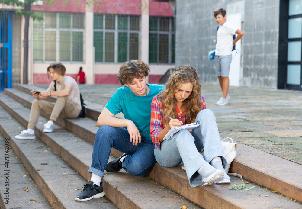 Teenager boy and girl sitting on stairs near school and doing homework.