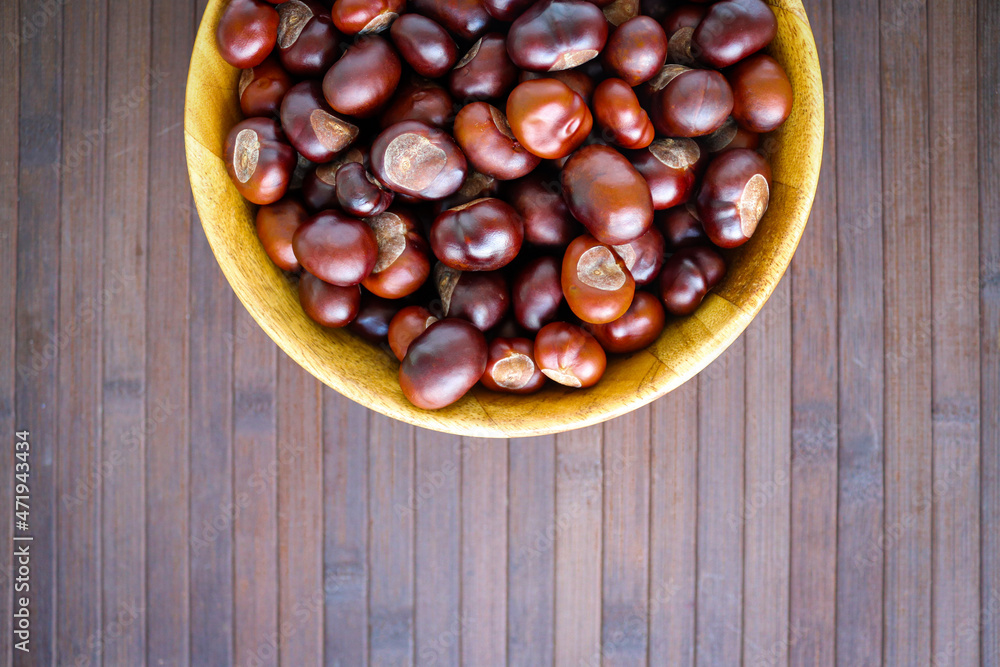 Obraz premium Chestnuts in a wooden bowl on wooden backgound