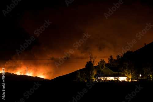 Fire and smoke near a house at the bottom of a hill during a wildfire