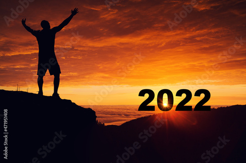 Man silhouette on the mountain top watching toward sunrise of 2022 new years and celebrate