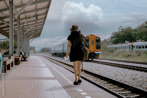 An Asian woman travels with a suitcase and a backpack in a railway line, a backpack and hat at the train station with travel idea travellers. Female tourists walk at the train station