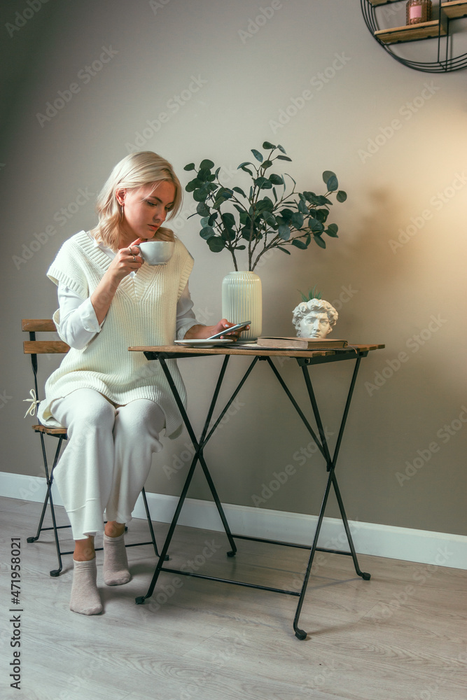A young girl sits at a coffee table with a phone and a cup of coffee in her hands
