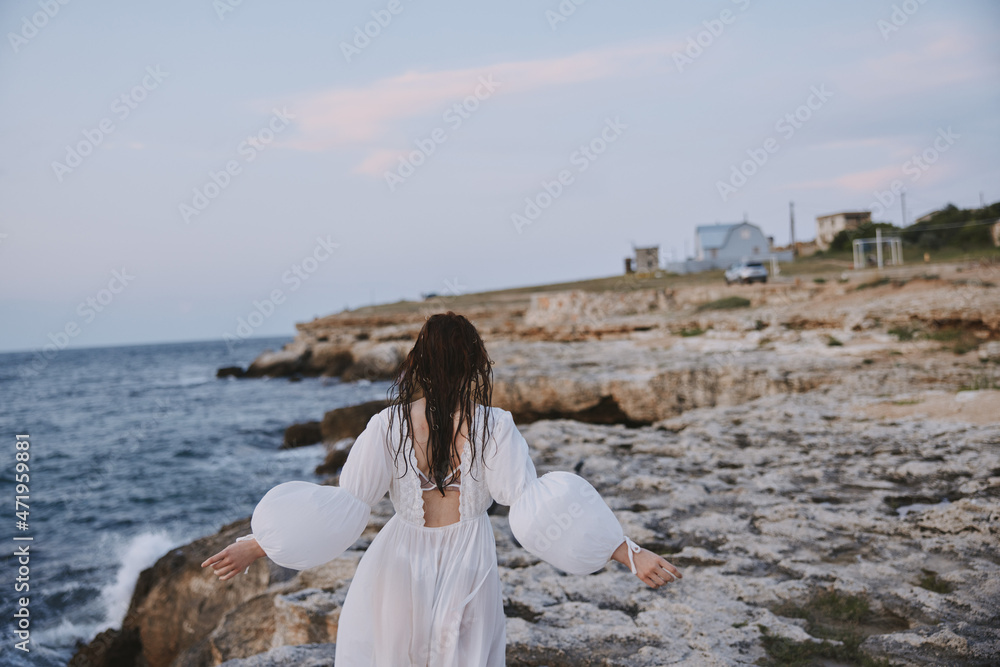 Woman in white dress walks on the beach stones back view Woman in white dress walks on the beach stones back view