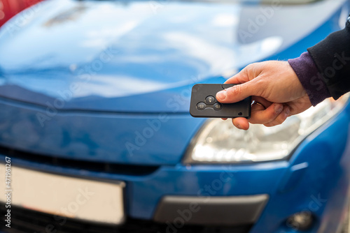 male hand in a business suit holds black car keys on a background of blue beautiful own car.
