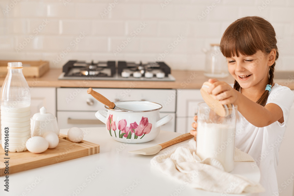 Portrait of happy smiling charming little girl baker preparing dough for baking, posing near table with ingredients, expressing optimism, like cooking alone, making surprise for mother. Portrait of happy smiling charming little girl baker preparing dough for baking, posing near table with ingredients, expressing optimism, like cooking alone, making surprise for mother.
