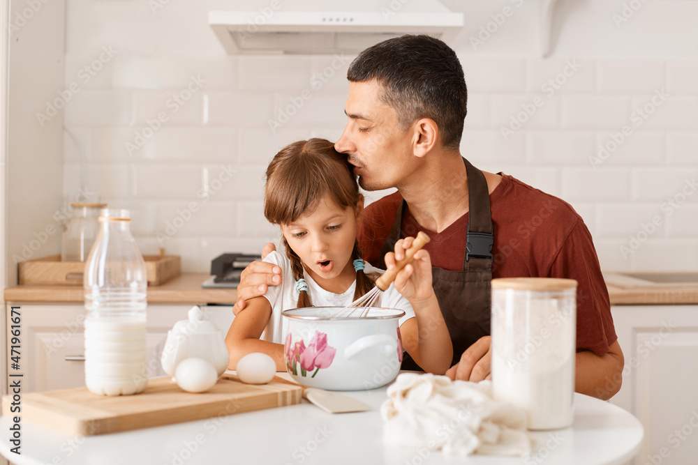 Indoor shot of happy lovely family posing in white kitchen, father kissing his daughter while making pie or cake together, father and child preparing tasty surprise for mother. Indoor shot of happy lovely family posing in white kitchen, father kissing his daughter while making pie or cake together, father and child preparing tasty surprise for mother.