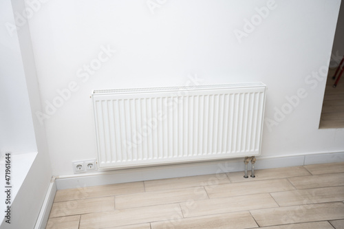 Heating radiator in a white room with laminated wooden floor