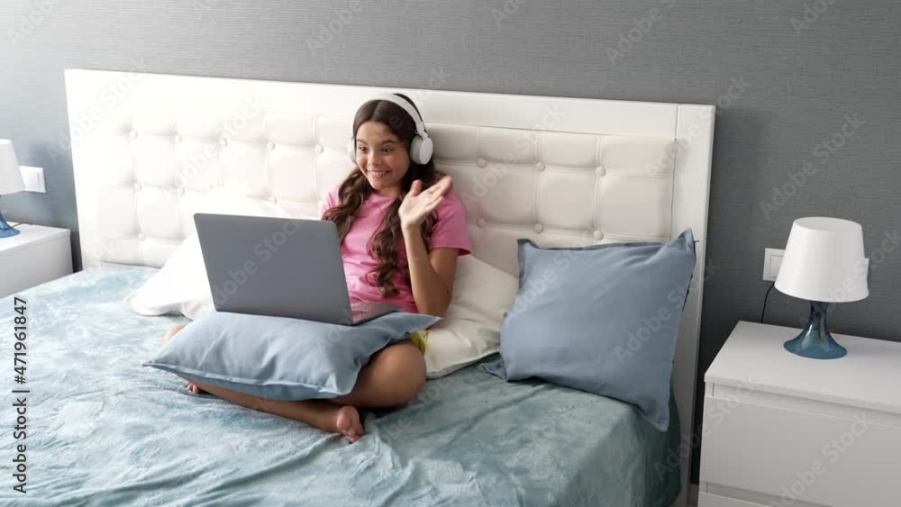 happy small girl in headphones started elearning with computer online in bed, childhood happy small girl in headphones started elearning with computer online in bed, childhood