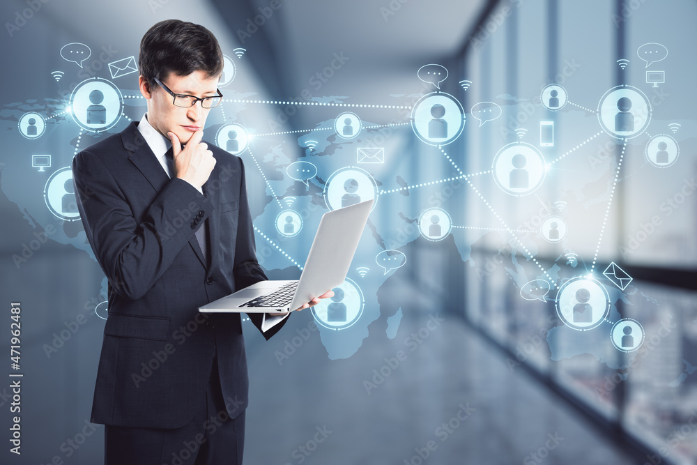 Portrait of attractive young european businessman looking at laptop in blurry office interior with glowing map and social connections hud screen. Communication and globalized business concept. Portrait of attractive young european businessman looking at laptop in blurry office interior with glowing map and social connections hud screen. Communication and globalized business concept.
