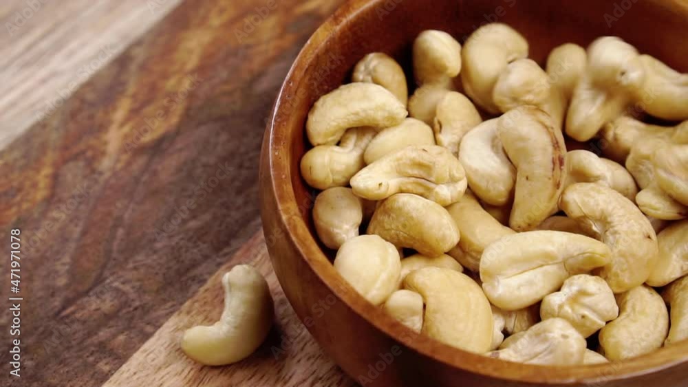 Falling dry cashew nuts in slow motion into a wooden rustic bowl. Raw organic kernels. Close-up Falling dry cashew nuts in slow motion into a wooden rustic bowl. Raw organic kernels. Close-up