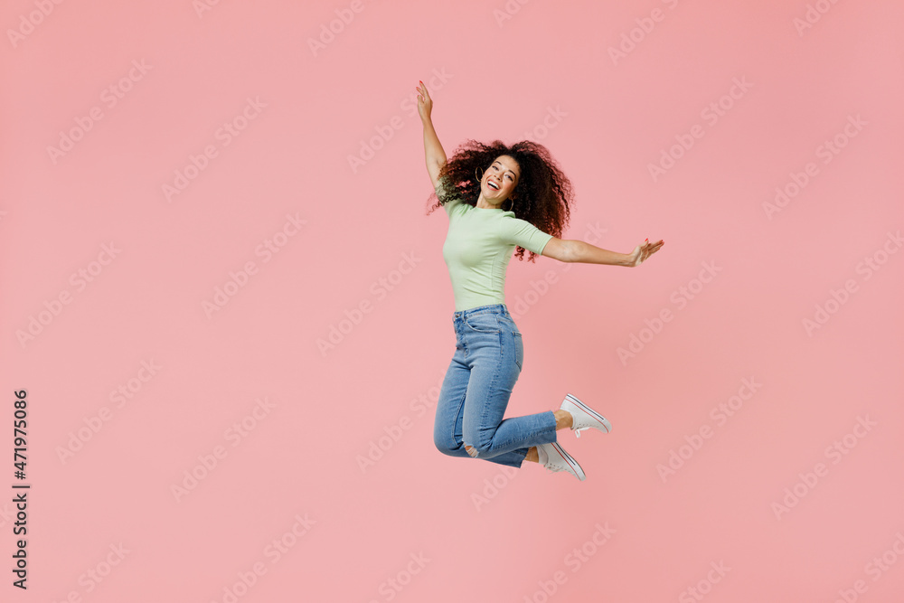 Full size body length fun young curly latin woman 20s wear casual clothes sunglasses jumping spreading hands keeps arm in flying gesture isolated on plain pastel light pink background studio portrait