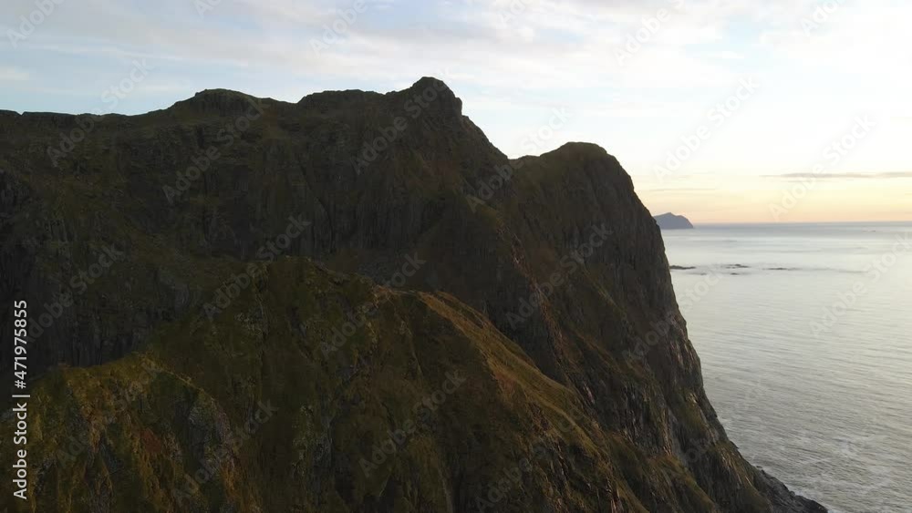 Aerial drone view of a massive steep mountain, rising from the ocean, sunset in Lofoten, Norway Aerial drone view of a massive steep mountain, rising from the ocean, sunset in Lofoten, Norway