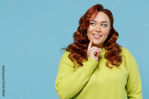 Young minded dreamful wistful chubby overweight plus size big fat fit woman wearing green sweater look aside on copy space isolated on plain blue background studio portrait. People lifestyle concept. photo